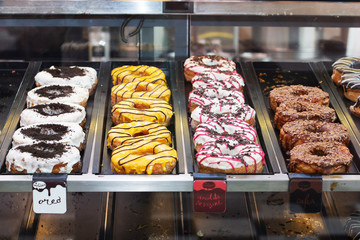 Colorful donuts with sprinkles in a restaurant's display case, sorted on a nirosta storage