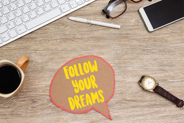 follow your dreams on speech bubble on office wooden table