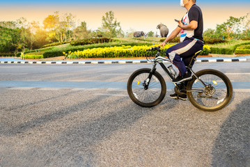 Chiang Mai: 11/05/2019; Tourist with face mask spotted renting a A man riding bicycle wears face mask with holding mobile phone in park