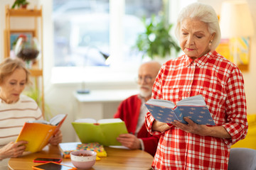 Serious grey haired woman standing with a book