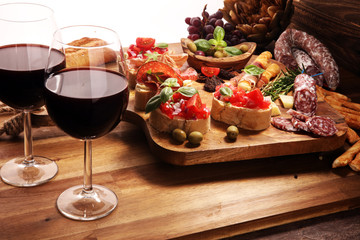 Traditional italian antipasto bruschetta appetizer with cherry tomatoes, cream cheese, basil leaves and balsamic vinegar on cutting board with prosciutto, salami, cheese
