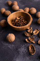 Cracked walnuts in wooden bowl and on black slate surface. Healthy nuts and seeds composition.