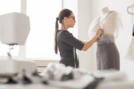 Dressmaker, tailor, fashion and showroom concept - Side view of female fashion designer measuring materials on mannequin in office