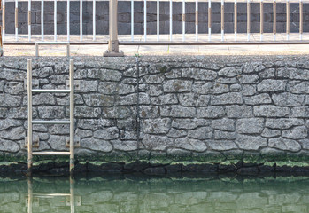 an emergrncy ladder stair on old stone wall near riverside.