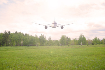 Fototapeta na wymiar Airliner over a green field and forest. Sunset.