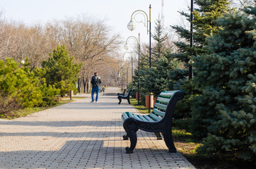 paved park alley leaving the distance. benches, lanterns and a man in the background.