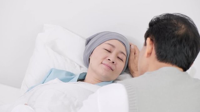 Asian senior man talking to his sick sleeping wife in bed in hospital. Senior life concept.