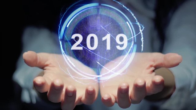 Female hands show a round conceptual hologram with text 2019. Unrecognizable woman in ashen white on a black background with future holographic technology