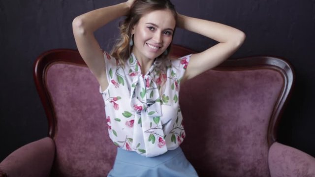 Young funny girl sitting on the couch in a beautiful dress dancing and laughing, spinning and having fun
