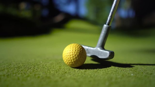 Mini Golf yellow ball with a bat near the hole at sunset