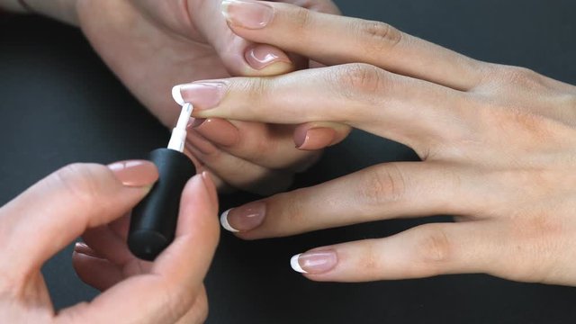 the manicurist paints the client's nails with  nail polish on a black background Painting nails. Female hands with beautiful french manicure