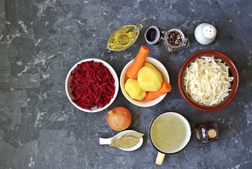 Ingredients for cooking borscht, traditional hot Russian soup with beetroot, cabbage and potatoes on a dark gray concrete background.