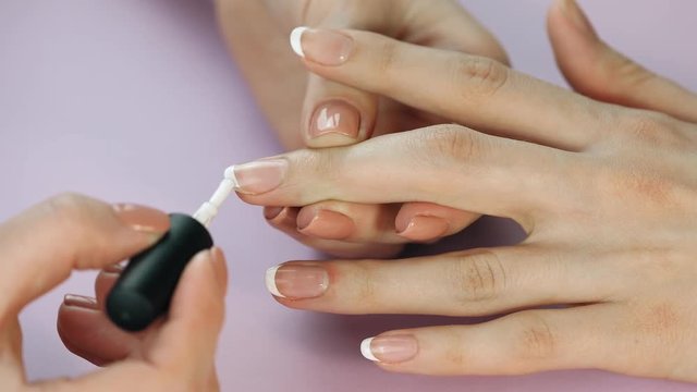 the manicurist paints the client's nails with  nail polish on a lite purple background Painting nails. Female hands with beautiful french manicure