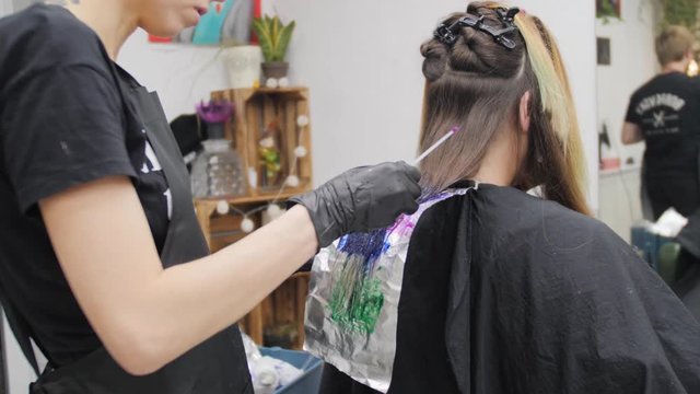 Professional woman hairdresser making creative hairstyle to girl in beauty salon.