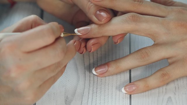 the manicurist paints the client's nails with  nail polish on a white background Painting nails. Female hands with beautiful french manicure