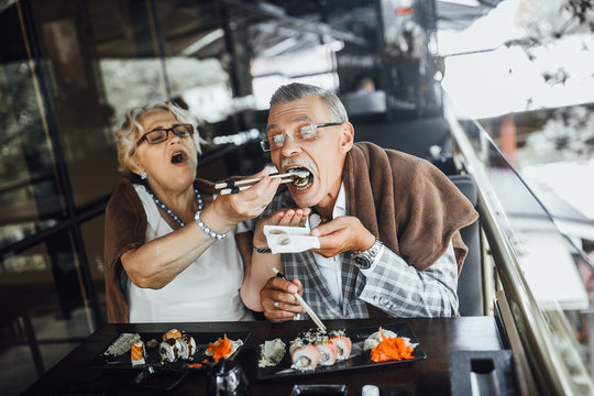 Lovely Seniors Couple Eating Sushi With Red Fish And Sitting At Summer Terrace