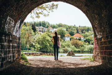 Young woman with cotton bag on shoulder standing in front of tunnel. Walls covered with grafitti. Prague, Czech Republic