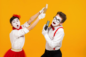 portrait of mime couple artist quarreling and reading book isolated on yellow background