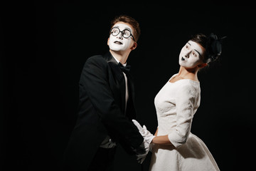 portrait of couple mime on black background. man in tuxedo and glasses and woman in white dress