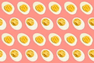Rows of many halves of boiled eggs on a coral background