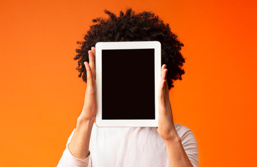 Young man hiding his face behind digital tablet