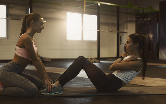 Trainer helping woman doing abs exercise on mat in gym