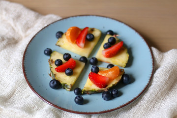 Plate with pineapple 'pizzas' - slices of pineapple with strawberries, tangerines and blueberries. Selective focus.