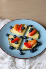 Plate with pineapple 'pizzas' - slices of pineapple with strawberries, tangerines and blueberries. Selective focus.