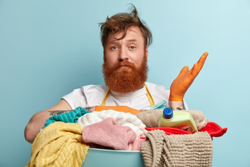 Headshot of hesitant red haired bearded man raises hand with doubt, stands in front of big basket...