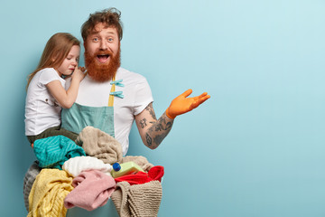 Laundry and household concept. Delighted redhead man with thick beard, raises hand, carries small...
