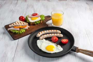 Fried eggs with sausage and vegetables on pan. Breakfast with orange juise and croissant on wooden rustic boards, food background.