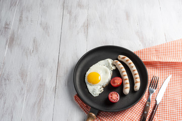 Fried eggs with sausage on pan. Breakfast on wooden rustic table, food background.