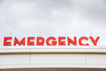 Naklejka premium A prominent red 3D all-caps lighted emergency directional sign and marker perched on the awning and canopy of the main hospital entrance.
