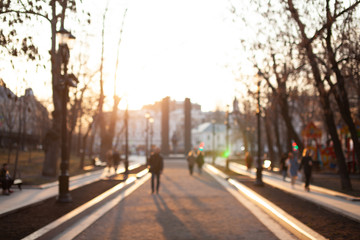 Evening walking in a beautiful city park on the sunset. Spring Promenade. People walking on the path. Blurred. Concept.
