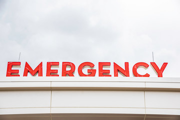 A prominent red 3D all-caps lighted emergency directional sign and marker perched on the awning and canopy of the main hospital entrance.