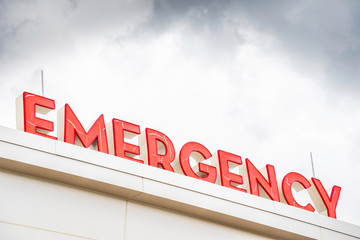 Naklejka premium A prominent red 3D all-caps lighted emergency directional sign and marker perched on the awning and canopy of the main hospital entrance.
