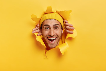 Glad handsome man with toothy smile, joyful expression, tears paper wall, feels glad to see...