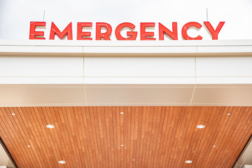 A very prominent all-caps 3D "emergency" sign letters in red on top of the canopy entrance of a medical hospital facility.