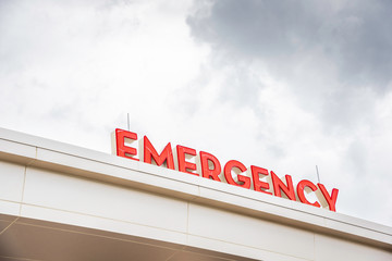 A very prominent all-caps 3D "emergency" sign letters in red on top of the canopy entrance of a medical hospital facility.