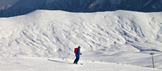 Skier downhill on snowy ski slope in sun winter evening