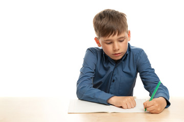 A left-handed child in a blue shirt, on a white isolated background, sits at the table and writes in his left hand. Copy space