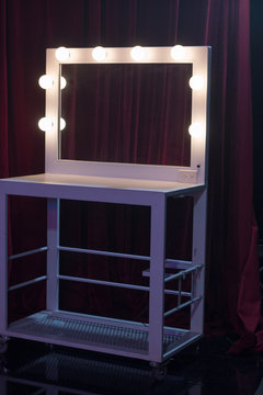 Make up mirror with lights backstage of a theater, or behind the scenes of a film, movie, or television production.   The white makeup mirror sit in front of a red curtain. Broadway or Hollywood feel.
