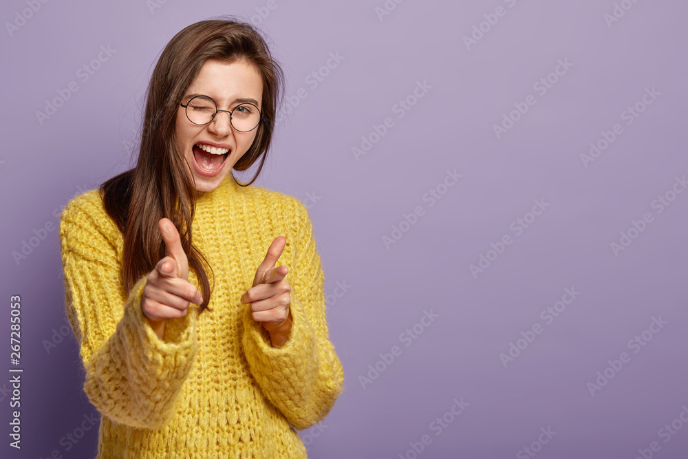 Wall mural joyous lovely female blinks eyes, exclaims from happiness, points at you, demonstrates her choice, f