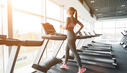 Young woman doing cardio training on treadmill near window