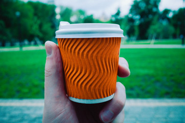 Paper cup for coffee. A small, orange glass of coffee is held by a man's hand