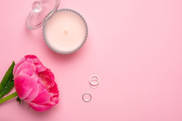 Beauty women's flat lay with piony flower, candle and rings with copy space for your text on pastel pink background.Fashion summer colour.
