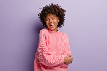 Sincere gentle feminine model expresses positive emotions and feelings, being glad to pose on camera for making photo, dressed in oversized pink sweater, shows white teeth, has healthy skin. - Powered by Adobe