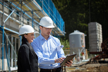 Two architects a man and a woman in construction in white helmets.