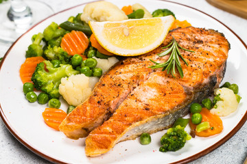 Grilled salmon steak with vegetables on white.