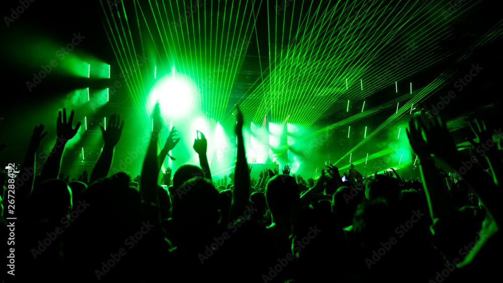 Wall mural Back view of audience with arms raised in front of stage at music concert.